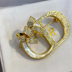 Broche con marco de lazo y letra con detalles de piedras