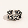 Anillo abierto con letras grabadas y bordes de cuerda